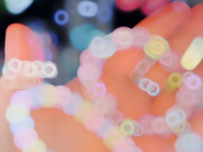 Pastel bead bracelets on a hand with colorful bokeh lights in the background, conveying a playful, dreamy mood