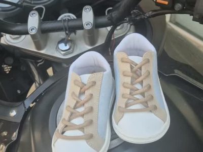 Pair of white and beige sneakers resting on a motorcycle gas tank, with handlebars and dashboard in the background.