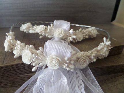 White ivory flower crown with small roses and ribbon, laid on wooden surface