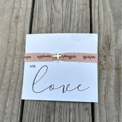 White card with 'with love' in cursive, a pink ribbon bracelet with a small gold cross laid across it on a wooden surface.