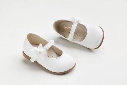 Pair of white Mary Jane shoes for a child with decorative flower on the strap and brown sole.