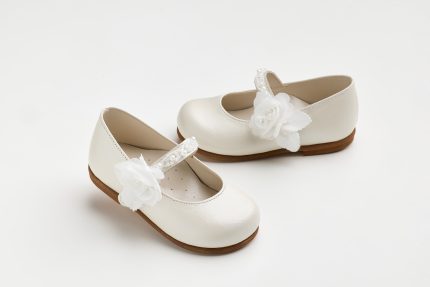 Pair of white kids' dress shoes with fabric flower embellishments and brown soles on a light background.