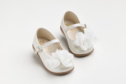 Pair of white children's Mary Jane shoes with large fabric flowers and brown soles on a white background.