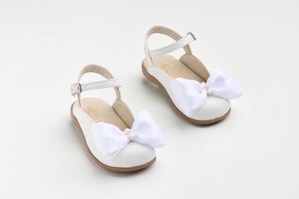 White baby sandals with ankle strap and large fabric bow on a white background, front view.