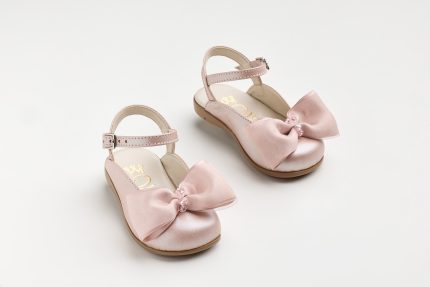 Pink baby sandals with satin bows and ankle straps on a white background.