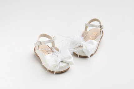 White children's sandals with ankle strap and feathered bows on a light background, front view