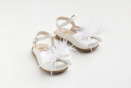 White toddler sandals with feather embellishments and bows on a light background, showing straps and buckle detail in beige sole.