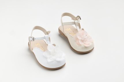 Pair of white dress sandals for a child with flower embellishments and tan soles photographed on a light background