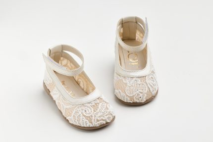 Two white lace baby shoes with ankle straps on a white surface.