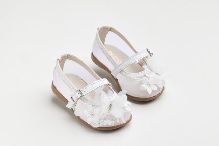 White baby dress shoes with lace, flower appliqués, and Velcro straps on a tan sole