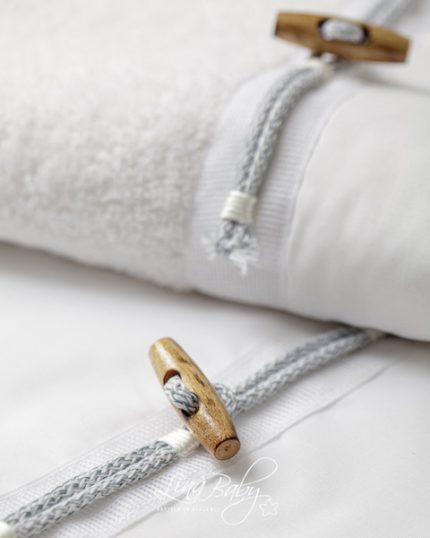 Close-up of a white baby blanket with gray braided drawstrings and wooden beads/toggles on the edge.