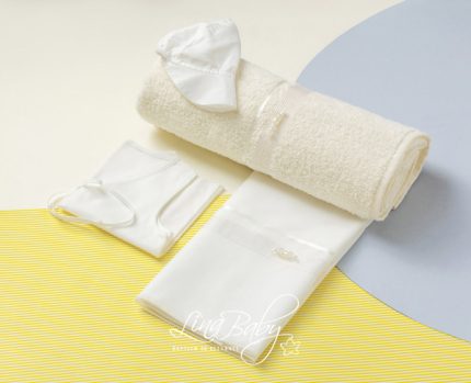 Spa towel set with a rolled beige towel, white cap, and face mask on a pastel backdrop.