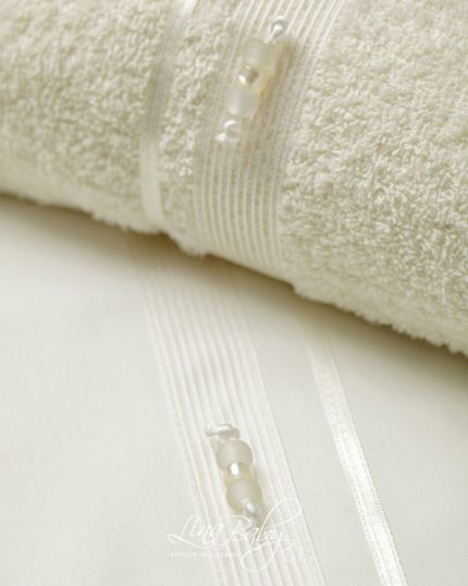 Close-up of a white fluffy bath towel featuring a decorative satin striped ribbon and small pearl-like buttons.