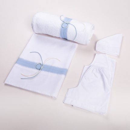 White bedding set with a light blue stripe, a rolled towel tied with blue cords, and white fabric pieces laid on a pale background.