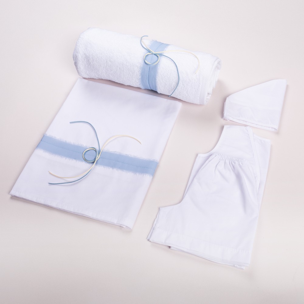 1300280-1000x1000 | La Vie en Rose White bedding set with a light blue stripe, a rolled towel tied with blue cords, and white fabric pieces laid on a pale background.