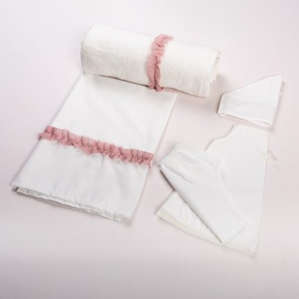 White baby linen set with pink ribbon trim: towel rolled with pink wrap, folded blanket, and white garments on a pale pink background.
