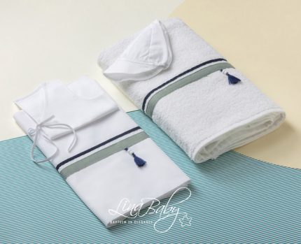 White baby clothing set and a rolled towel with blue tassels on a blue striped mat.