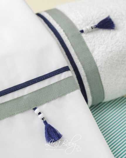 Close-up of decorative pillows with white fabric, teal and navy trim, and blue tassels resting on a turquoise-striped surface.