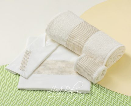 White bath towel set with rolled and folded towels and striped trim, displayed on a pale background with a green chevron surface.