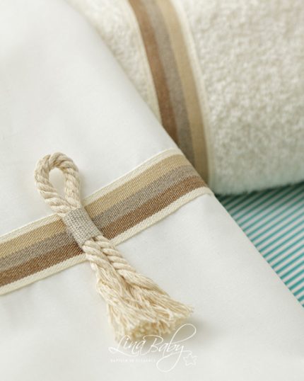 White fabric bundle tied with a beige striped ribbon and tassel on a teal-striped surface, close-up detail of packaging.