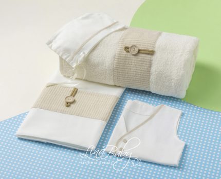 Set of white baby clothes with beige knit bands and wooden buttons, arranged on a blue polka-dot mat with a rolled towel in the background.