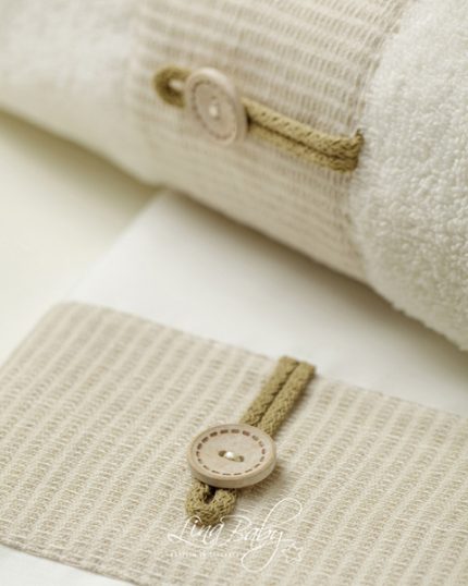 Close-up of beige fabric with a stitched seam and tan buttoned toggle detail, highlighting textile texture and craftsmanship.