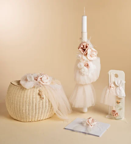 Wedding decor display with a tall candle wrapped in tulle and pink fabric flowers, beside a woven basket and a guest book fall-themed backdrop.