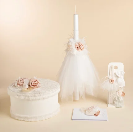 White wedding-themed display with a lace-topped cake, pedestal candle with tulle and pink roses, plus a gift box and invitation on a pale backdrop