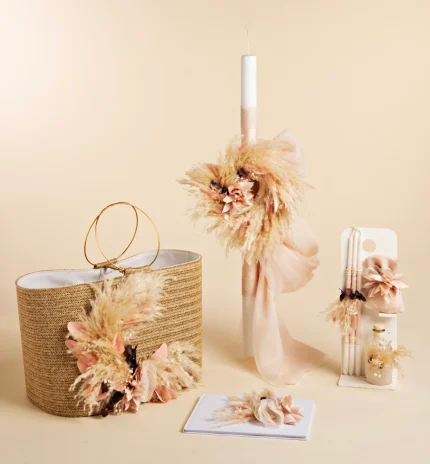 Beige still-life with a tall white candle wrapped in ribbons, surrounded by dried pampas grass and pale flowers near a woven basket.