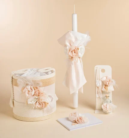 Pastel wedding decor: ivory candle wrapped with blush fabric and feathers, beside a woven basket with fabric flowers and ribbons.