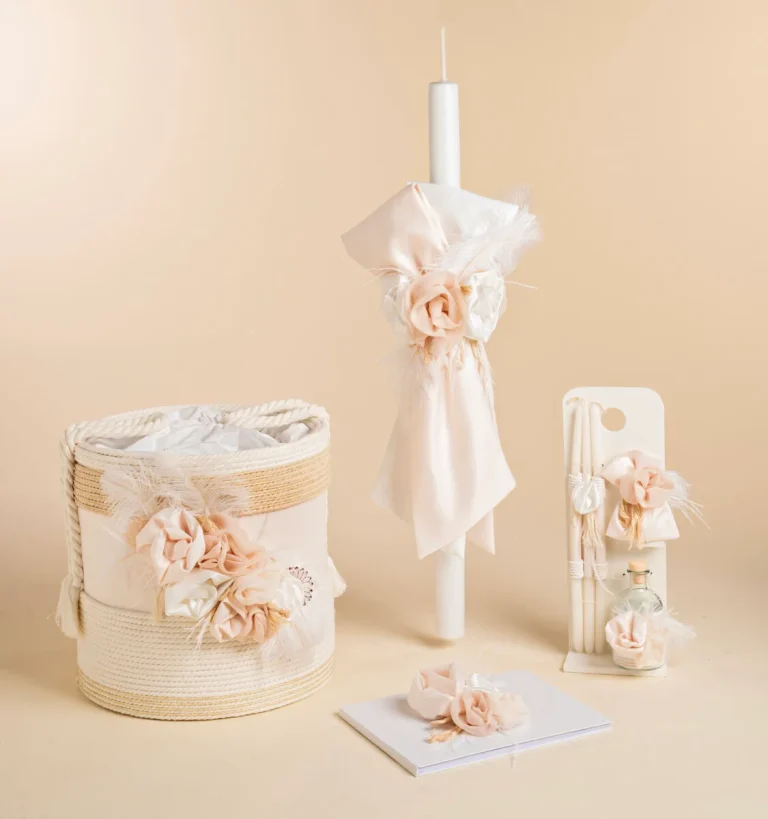 Pastel wedding decor: ivory candle wrapped with blush fabric and feathers, beside a woven basket with fabric flowers and ribbons.