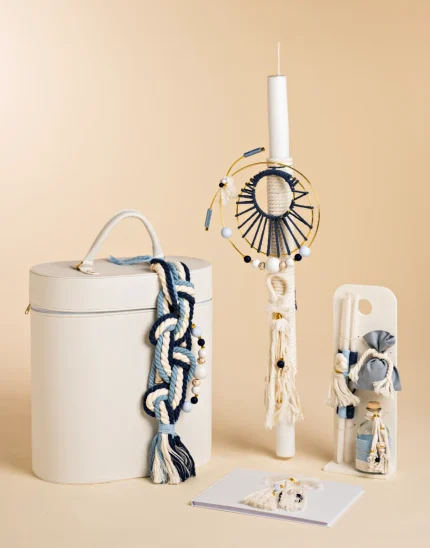 Boho-themed decor items: a white cylindrical container with a blue-and-white rope tassel, a candle with a circular woven ornament, and a white display stand with tassel accents.