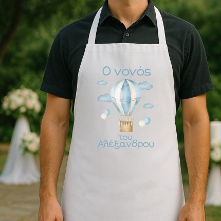 Person wearing a white apron with a blue hot-air-balloon illustration and light-blue Greek text, outdoors.