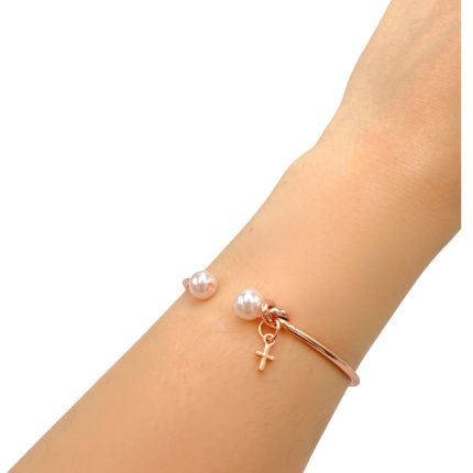 Rose-gold bracelet with two pearls and a small cross charm worn on the wrist.