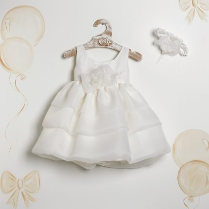 White baby/toddler formal dress with a layered, puffy skirt on a wooden hanger against a light backdrop with balloon decorations.