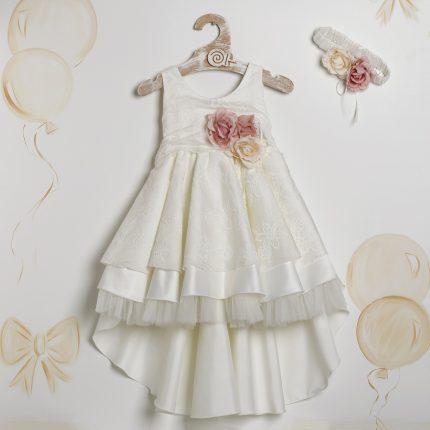 White lace dress for a girl with pink and cream flowers at the waist, hanging on a wooden hanger.