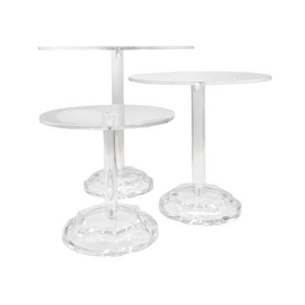 Three clear acrylic cake stands at varying heights with round tops and wide bases, set side by side.