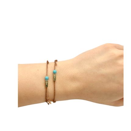 Two brown string bracelets on a wrist, each with turquoise bead and a small gold rectangular charm with a cross.