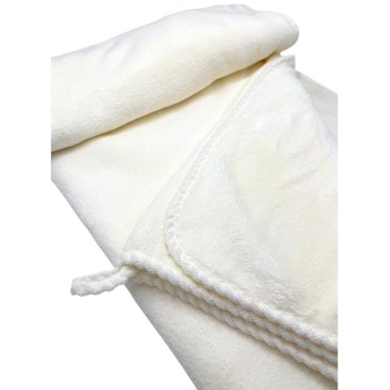 Close-up of a soft white plush blanket with a folded corner and braided edge edge details.
