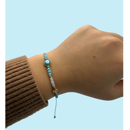 Close-up of a wrist wearing a turquoise bead bracelet with a small cross charm, set against a light blue background.