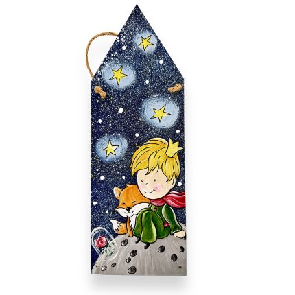 Decorative bookmark showing a blond boy in a green outfit and red scarf sitting on a gray asteroid with a fox, under a starry night sky and white stars.