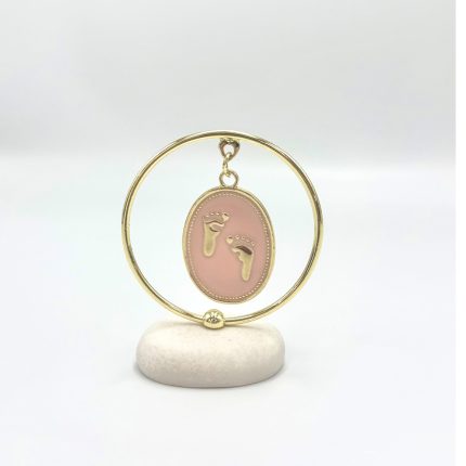 Gold circular frame with pink oval pendant featuring baby footprints, displayed on a white stone base.
