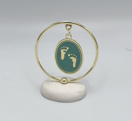 Gold circular hoop with a teal oval pendant showing two gold footprints, suspended from a small ring on the hoop.