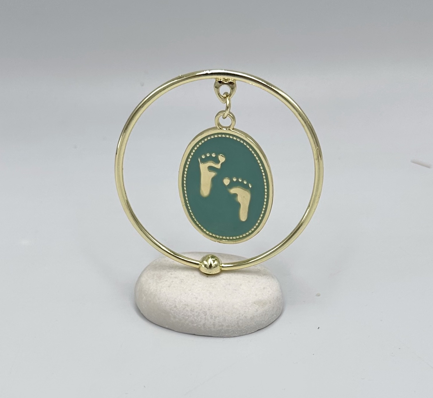 64D70BD3-DE41-D02E-472D-01997F9230AA_11 | La Vie en Rose Gold circular hoop with a teal oval pendant showing two gold footprints, suspended from a small ring on the hoop.