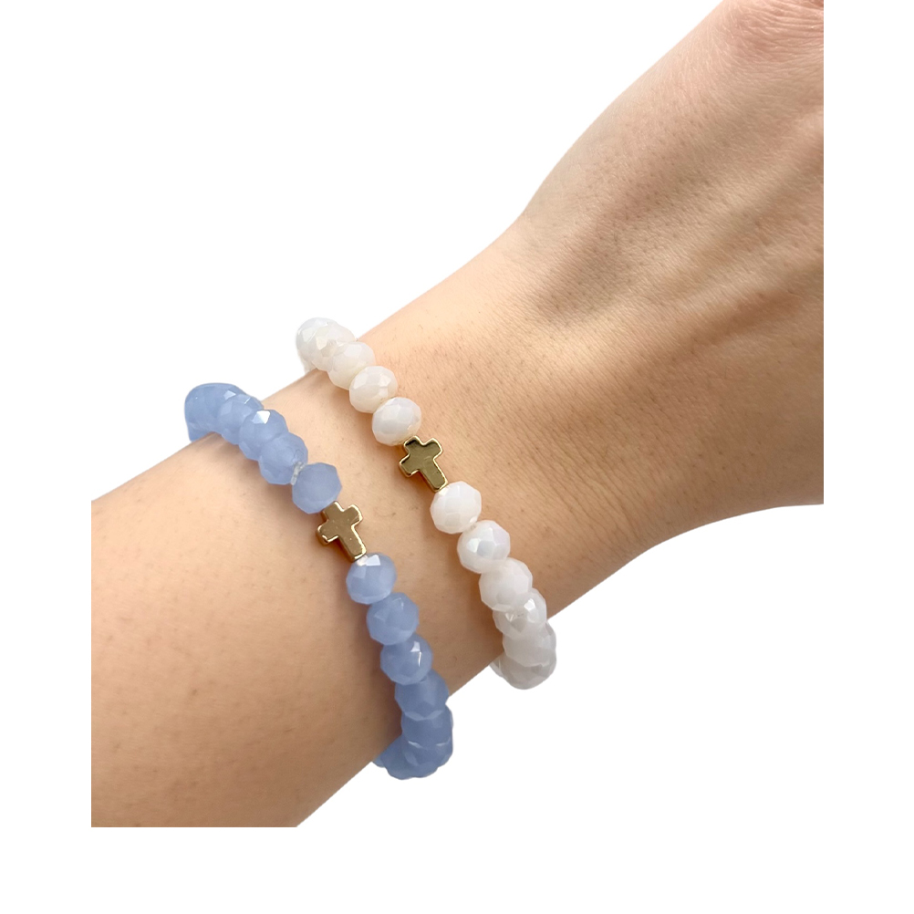 ADC556C4-BFCC-D794-3BF4-019D05FD7D79_21 | La Vie en Rose Two beaded bracelets on a wrist: one blue faceted strand and one white faceted strand, each with a small gold cross charm.