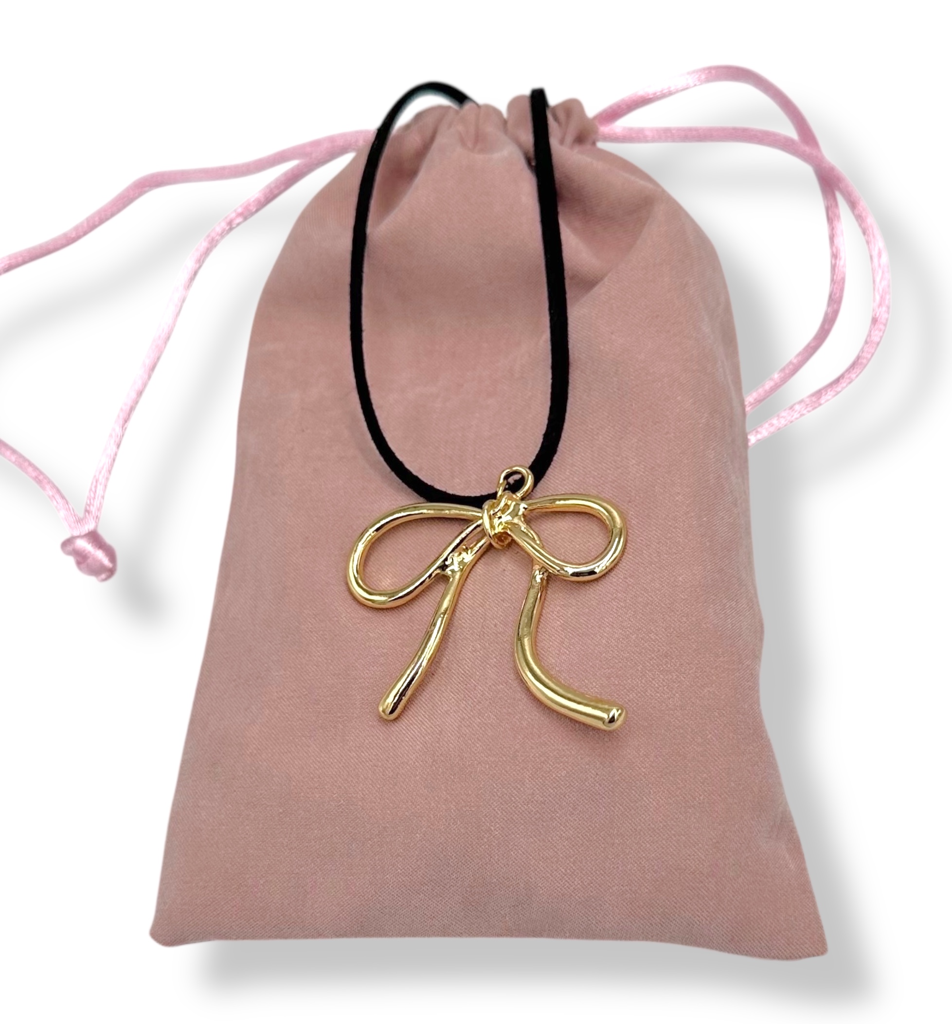 DB529B4C-391E-D4FA-4D91-019A1147B05D_21 | La Vie en Rose Pink velvet drawstring pouch with pink cords and a gold bow-shaped pendant resting on it.