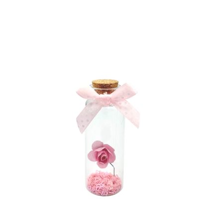 Clear glass bottle with a cork stopper, pink bow, and a pink artificial rose suspended above pink filler beads inside.