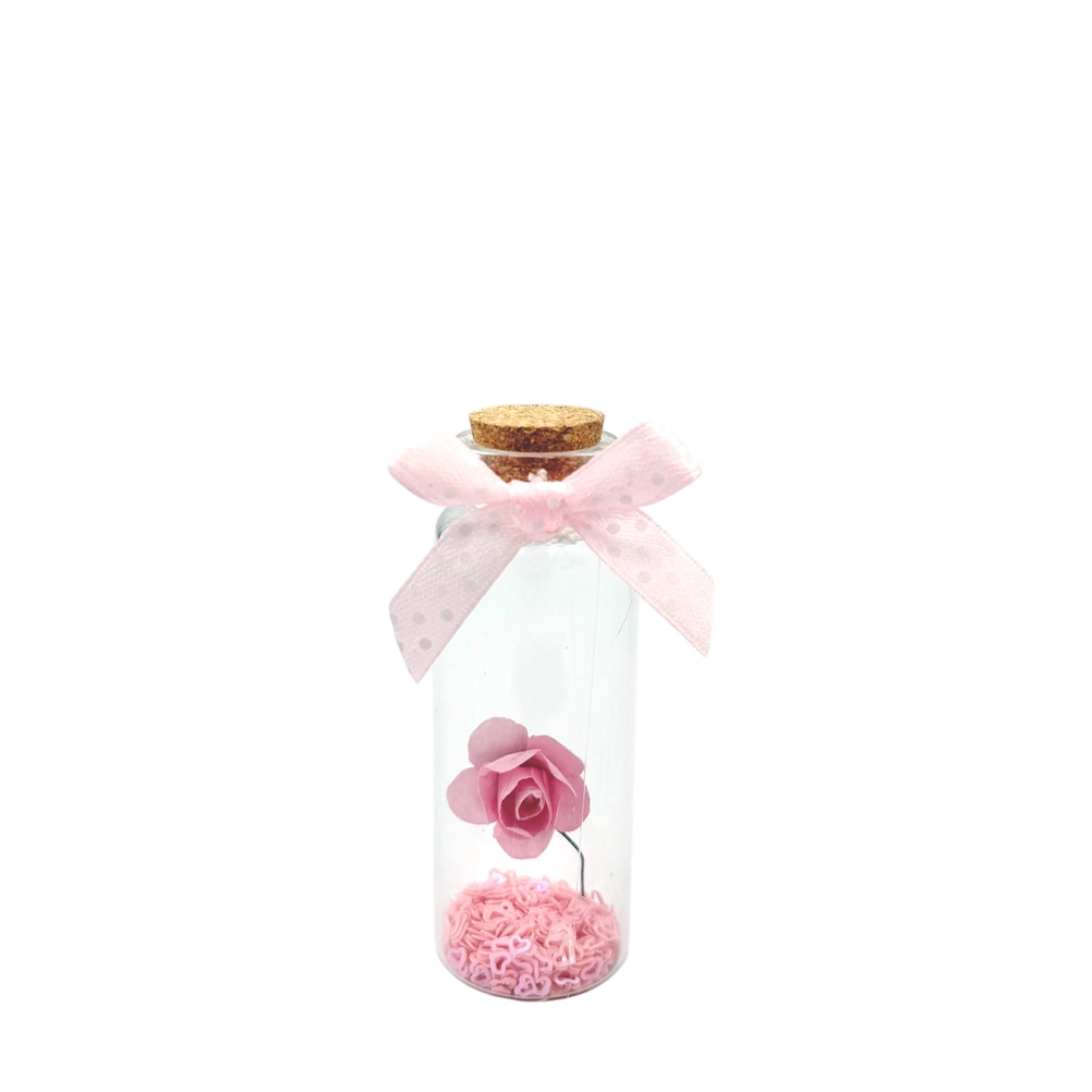 FC8B004A-4832-70F8-6859-019CFC1C63C5_1 | La Vie en Rose Clear glass bottle with a cork stopper, pink bow, and a pink artificial rose suspended above pink filler beads inside.