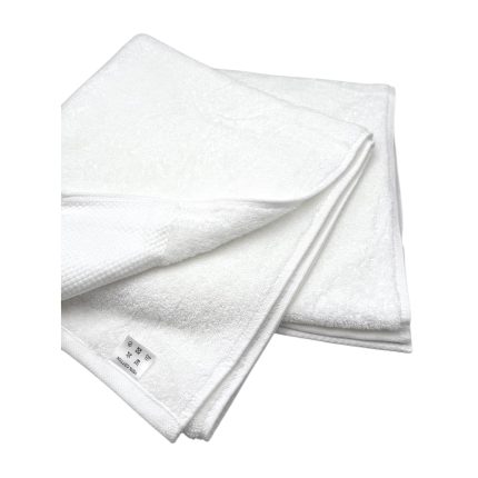 Two fluffy white bath towels folded neatly, stacked with a small care tag visible at the edge