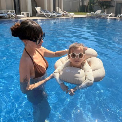Woman in a brown bikini helps a young girl sit on a gray inflatable float in a bright blue pool, sunny day.